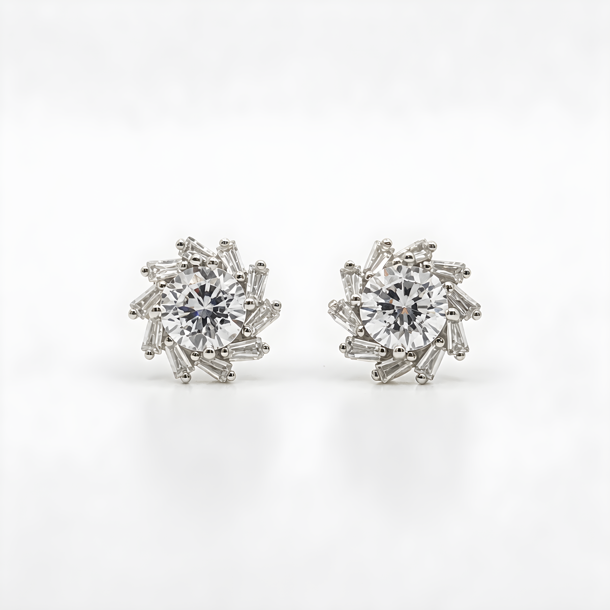 A pair of sterling silver stud earrings featuring a central round clear gemstone surrounded by a halo of baguette-cut clear stones.
