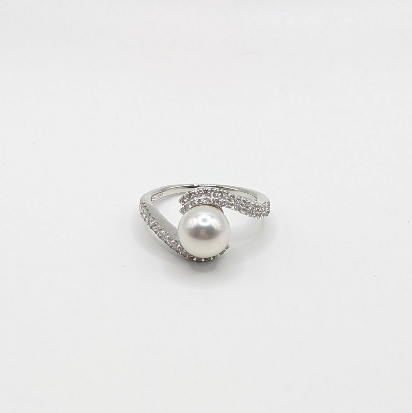 A silver-toned ring featuring a single lustrous white pearl at the center, surrounded by small clear stones along the band, set against a plain white background.