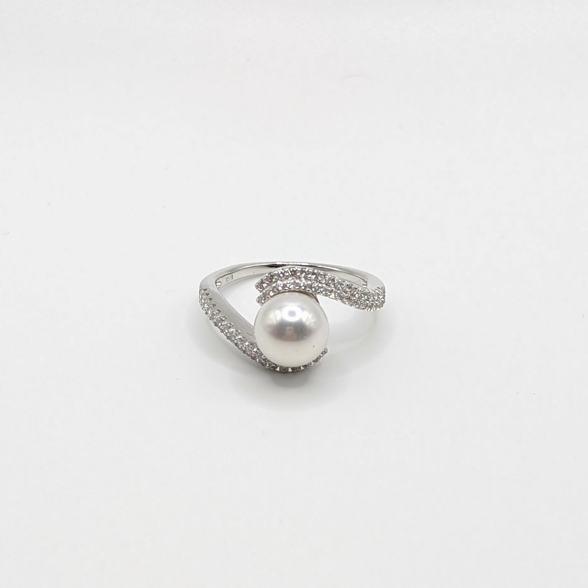 A silver-toned ring featuring a single lustrous white pearl at the center, surrounded by small clear stones along the band, set against a plain white background.