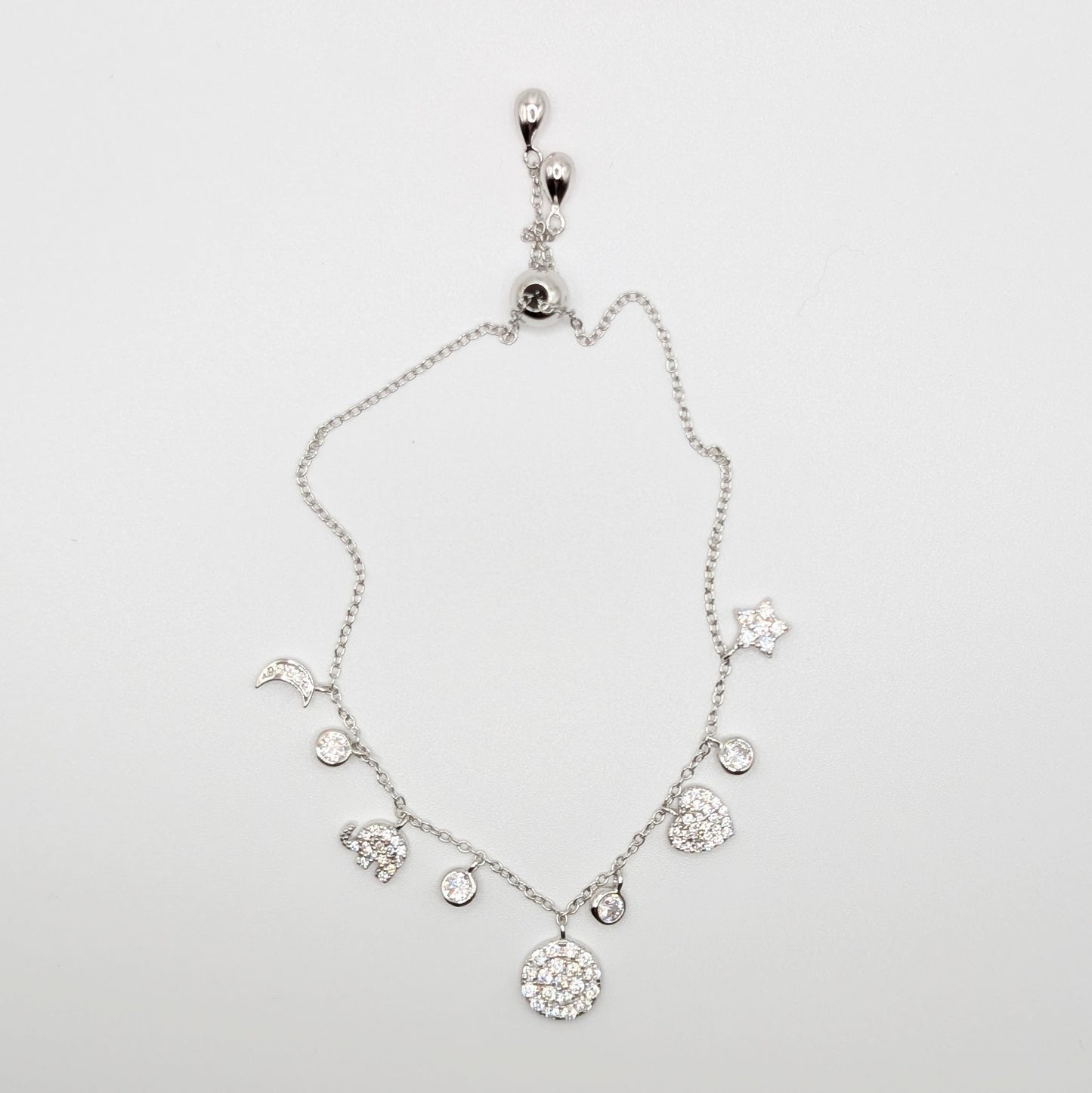 A silver-toned celestial charm bracelet with clear zircon-encrusted charms including a moon, sun, stars, hearts, and a large round flower.