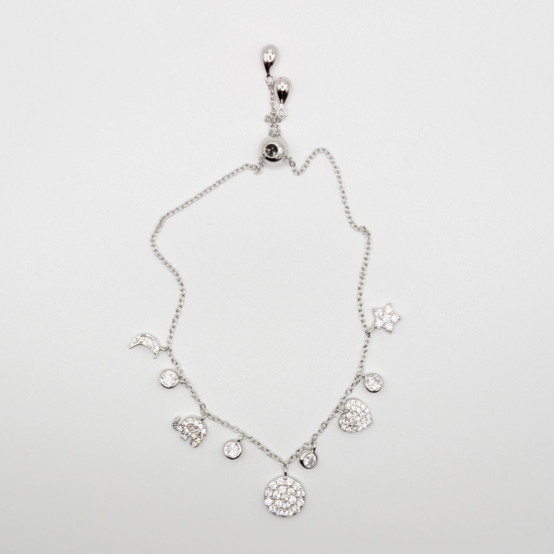 A silver-toned celestial charm bracelet with clear zircon-encrusted charms including a moon, sun, stars, hearts, and a large round flower.