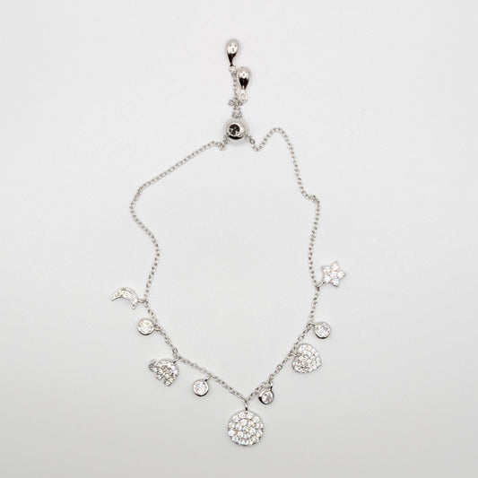 A silver-toned celestial charm bracelet with clear zircon-encrusted charms including a moon, sun, stars, hearts, and a large round flower.