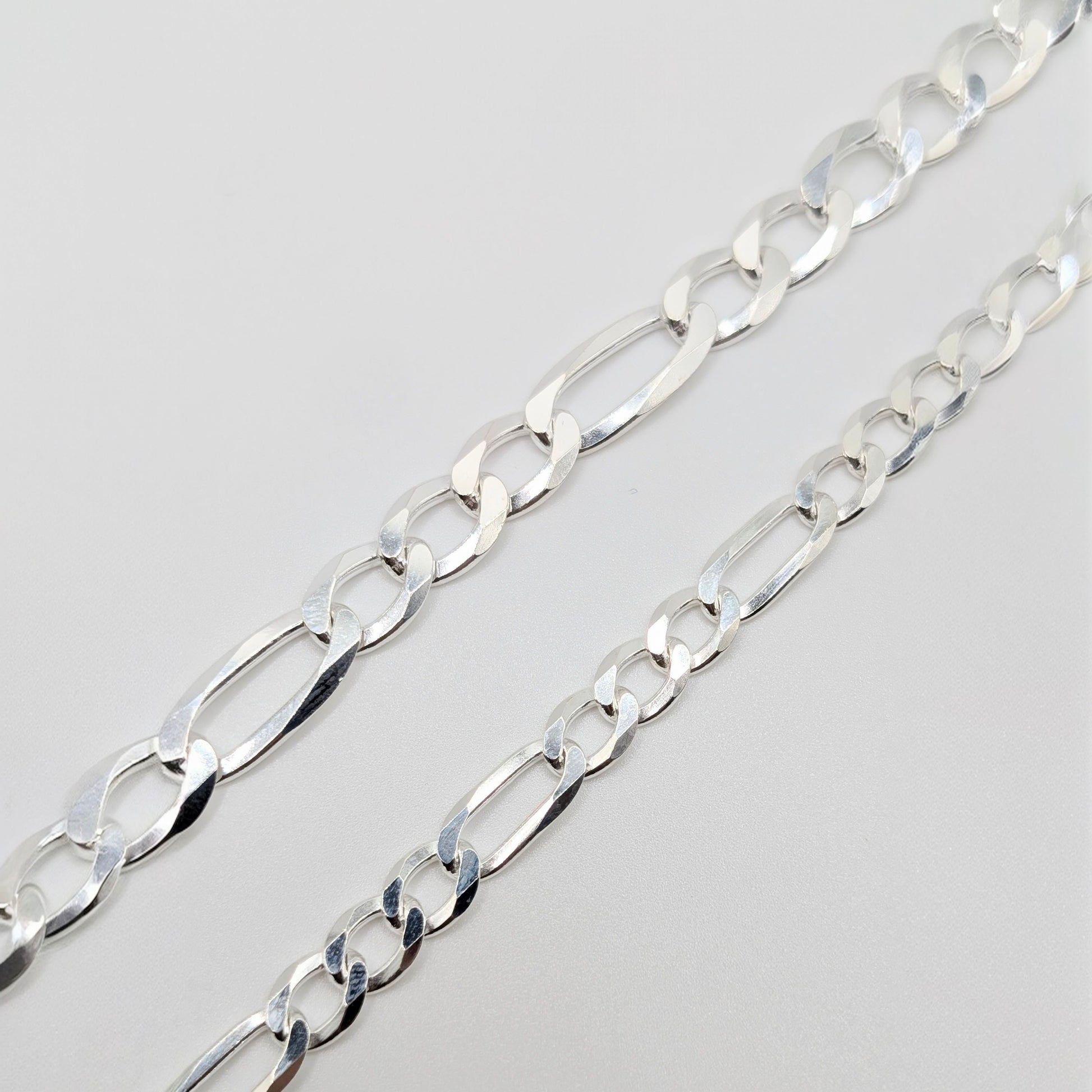 A close-up of a polished silver Figaro chain bracelet, showing the interlocking oval links.