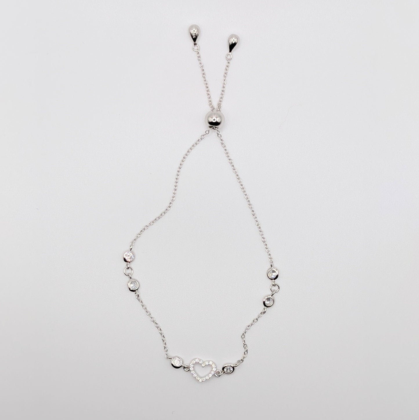 A delicate silver chain bracelet with a heart-shaped charm and small silver beads.