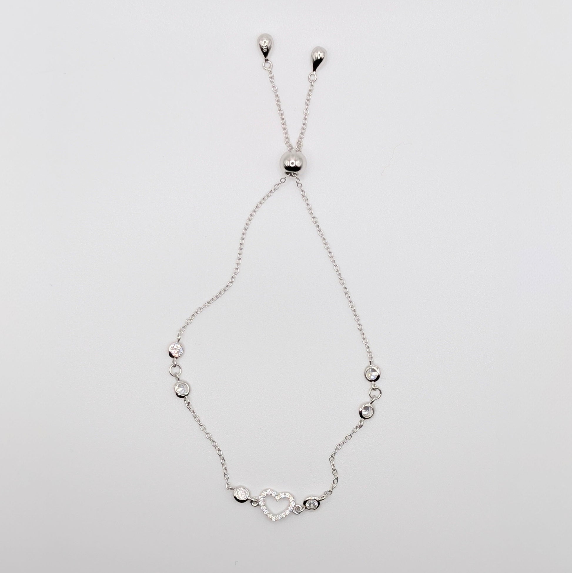 A delicate silver chain bracelet with a heart-shaped charm and small silver beads.