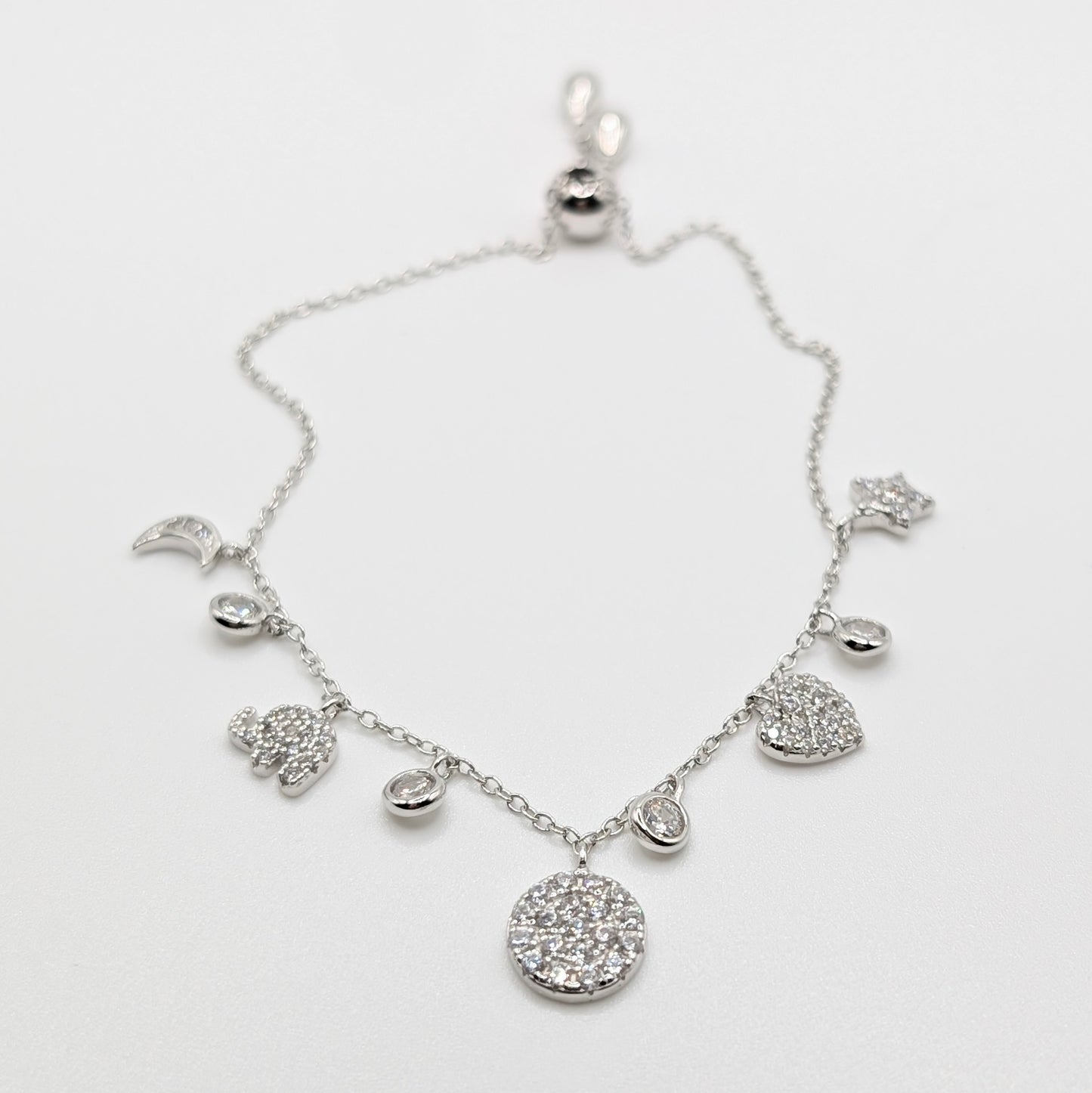 A silver-toned celestial charm bracelet with clear zircon-encrusted charms including a moon, sun, stars, hearts, and a large round flower.