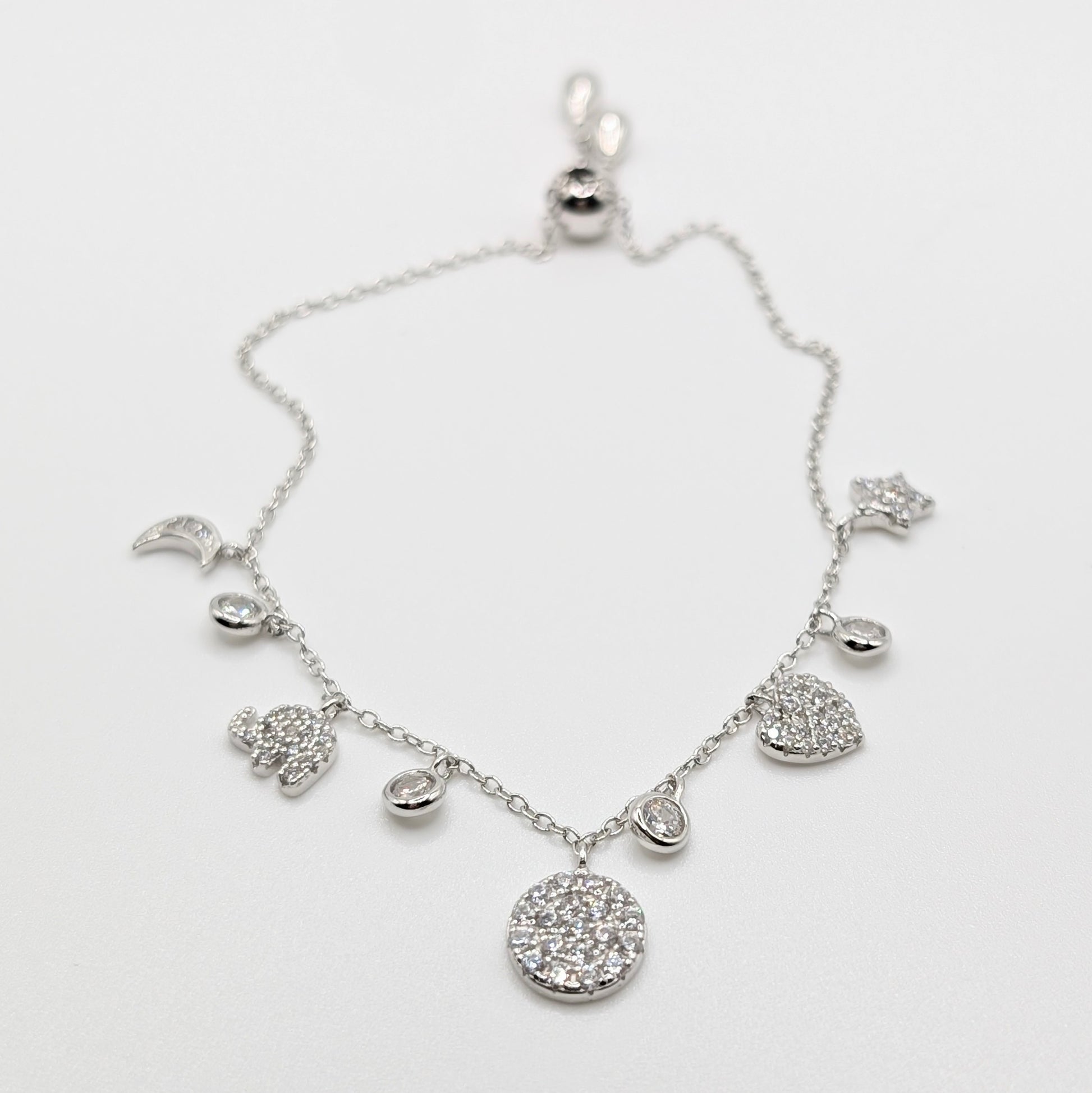 A silver-toned celestial charm bracelet with clear zircon-encrusted charms including a moon, sun, stars, hearts, and a large round flower.