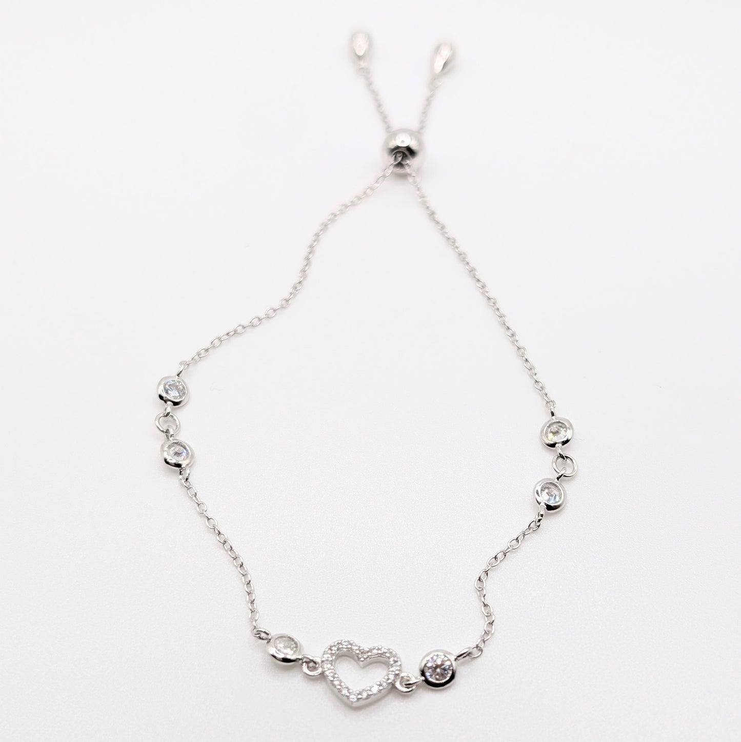 A delicate silver chain bracelet with a heart-shaped charm and small silver beads.