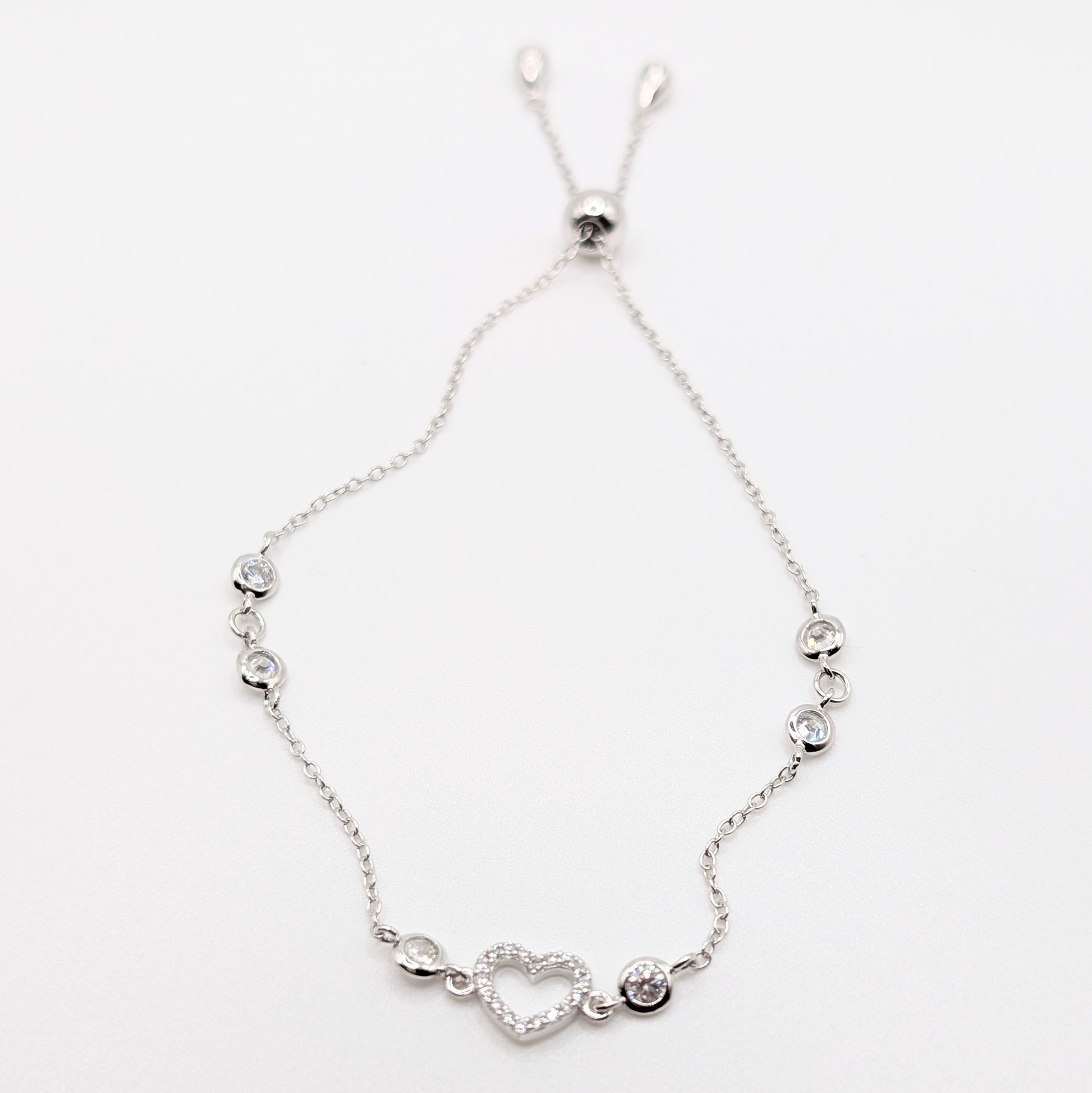 A delicate silver chain bracelet with a heart-shaped charm and small silver beads.