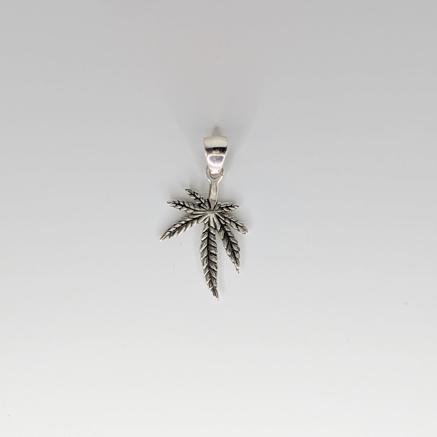 A silver pendant shaped like a cannabis leaf, suspended against a plain light gray background.