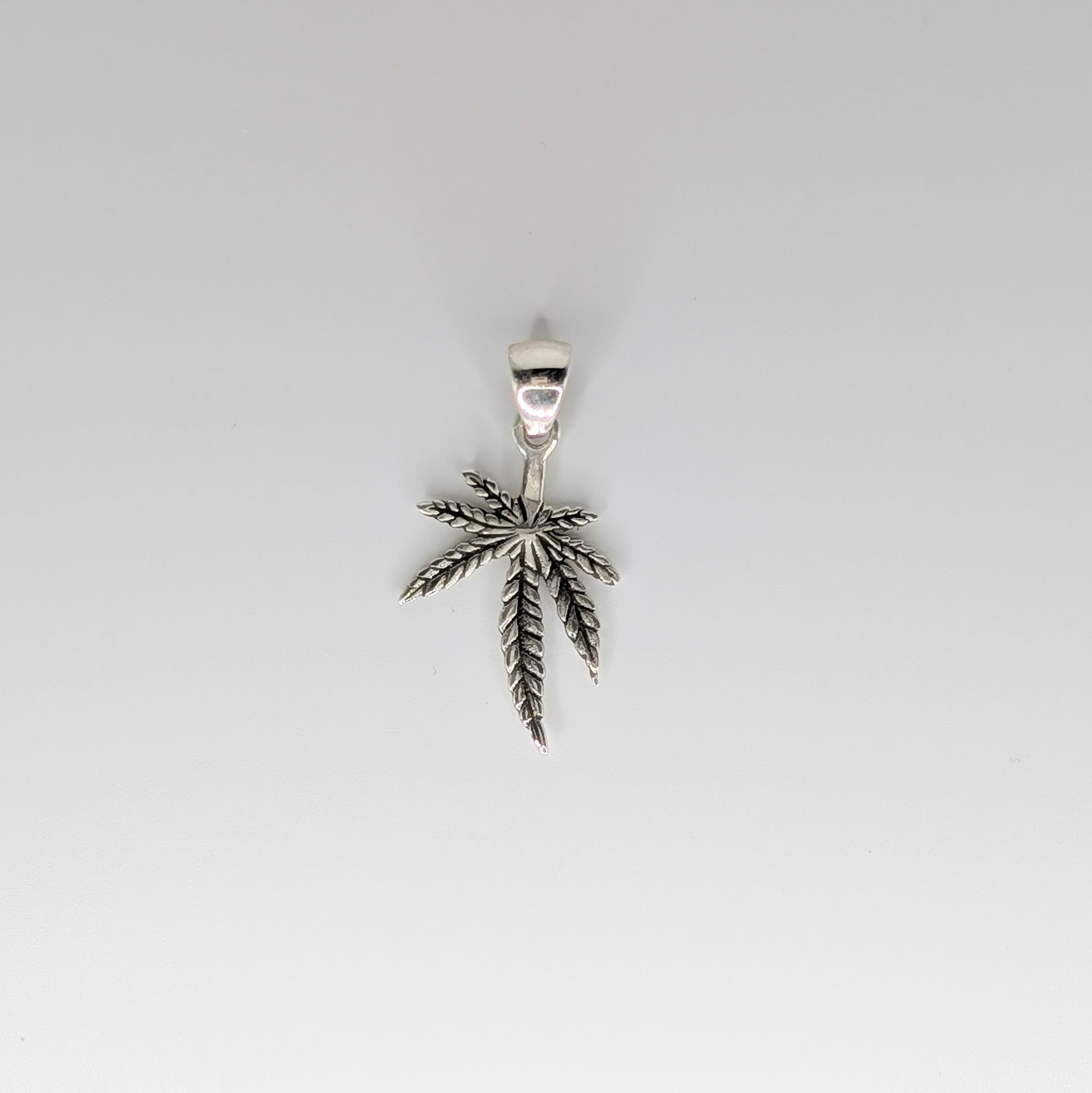 A silver pendant shaped like a cannabis leaf, suspended against a plain light gray background.