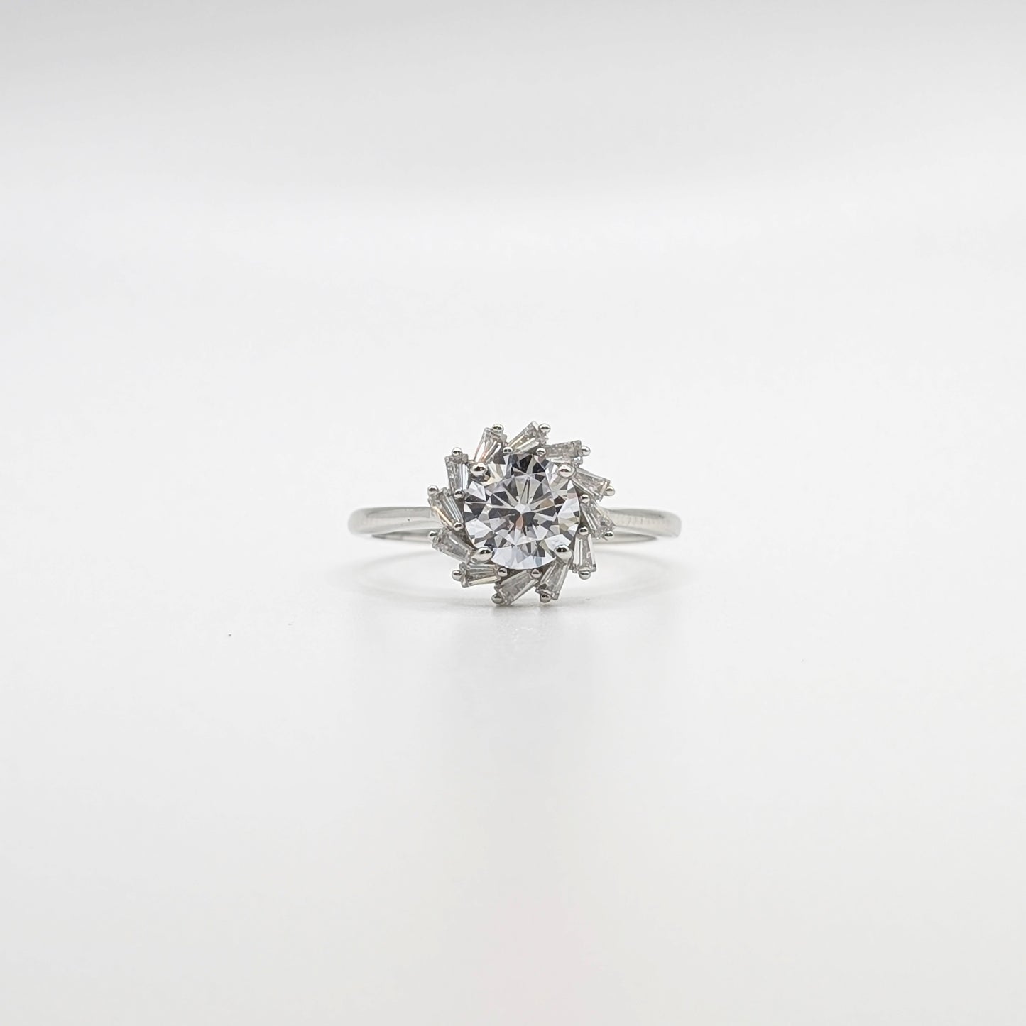 A silver-toned ring featuring a round clear gemstone surrounded by a cluster of smaller marquise-cut stones, set against a seamless white background.
