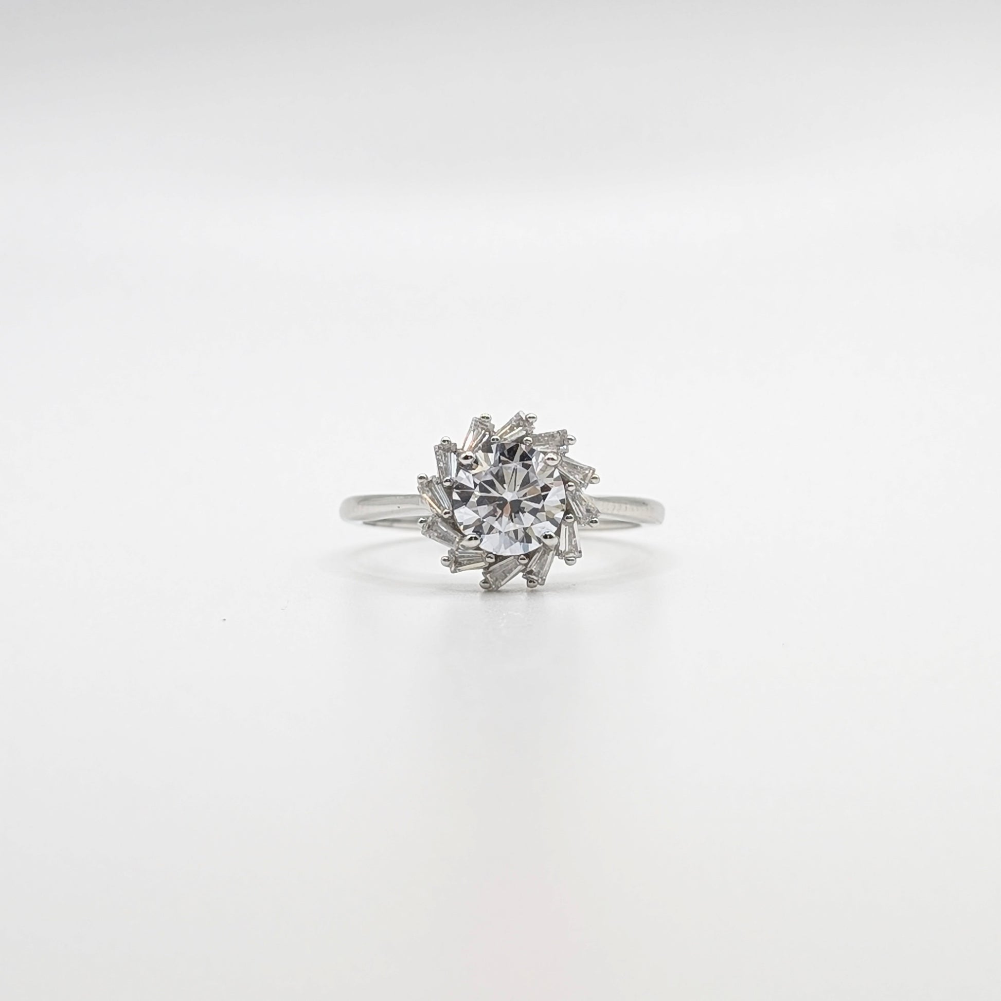 A silver-toned ring featuring a round clear gemstone surrounded by a cluster of smaller marquise-cut stones, set against a seamless white background.