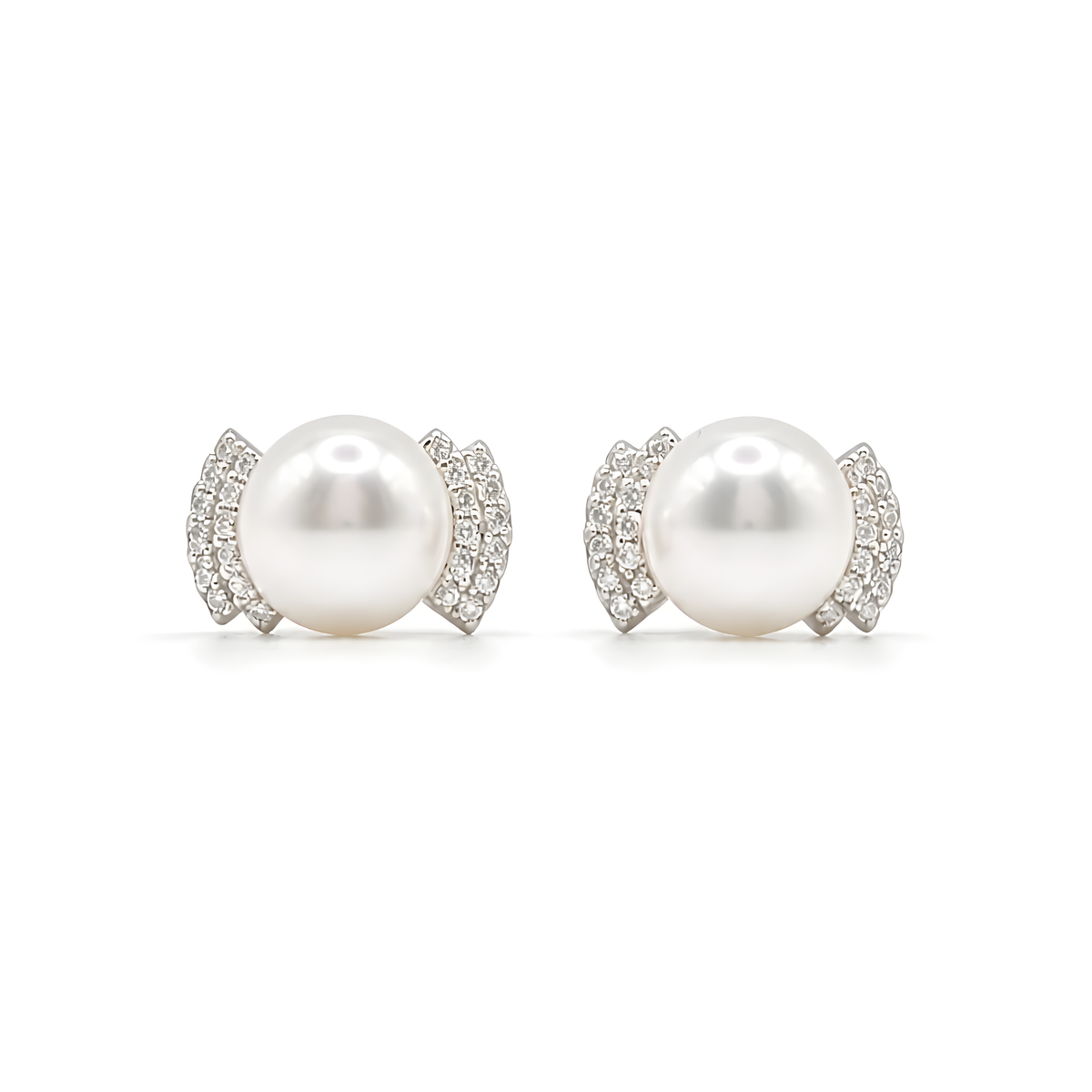 A pair of stud earrings featuring a large white pearl surrounded by a curved halo of small clear pavé stones in sterling silver.